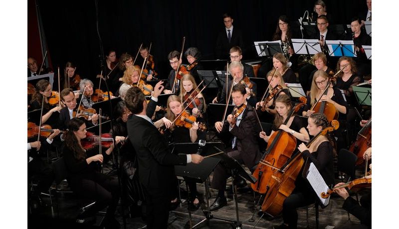 Ein Ausschnitt von Orchestermusikern mit dem Dirigenten während dem Konzert.
